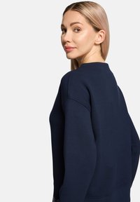 Sweat-shirt bleu marine avec un col rond, des manches longues et un tissu texturé présentant un motif contrastant à l'ourlet.