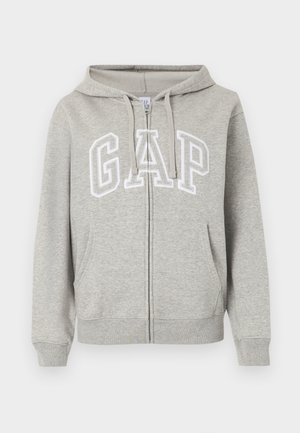Sweat à capuche zippé gris clair avec poches avant, capuche à cordon de serrage et grandes lettres "GAP" blanches en contour sur la poitrine.