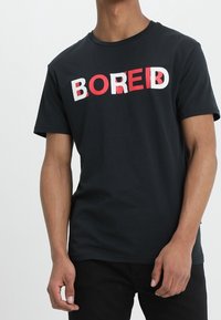 T-shirt in cotone nero con la parola "BORED" in grassetto bianco e rosso. Maniche corte e design classico a girocollo.