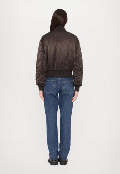 Brun bomberjakke med en glanset tekstur, ribbede sømmer og mansjetter, sammen med løse blå jeans og svarte platå sko. Enkelt design, uten mønstre.