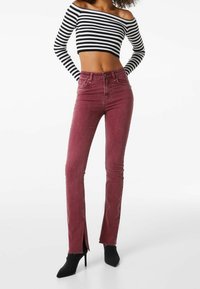 Höga maroon jeans med sidsspringor, tillverkade av bomullsdenim, kombinerade med en svartvit randig off-shoulder crop-top.