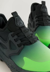 Zwart-groene sportschoenen met een soepel verloop aan de bovenkant, met textuuraccenten, een gevoerde kraag, vetersluiting en logodetail.