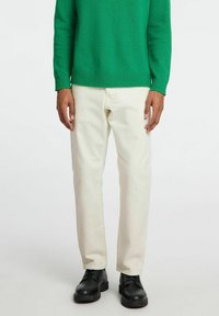 Maglione verde a maglia, pantaloni color crema, scarpe nere. Il maglione ha polsini e orlo a coste; i pantaloni sono a gamba dritta con una texture liscia.