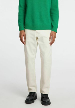 Pull en maille verte, pantalon beige, chaussures noires. Le pull présente des poignets et un ourlet côtelés ; le pantalon est droit avec une texture lisse.