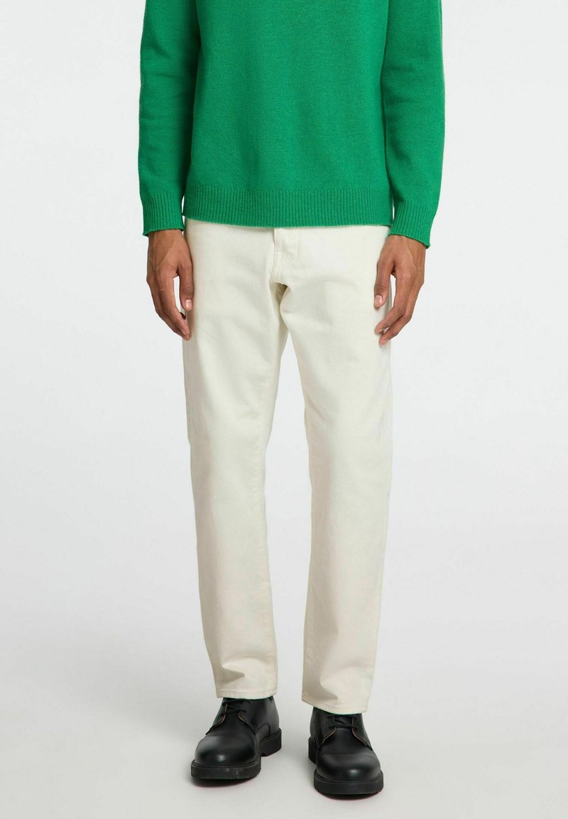 Maglione verde a maglia, pantaloni color crema, scarpe nere. Il maglione ha polsini e orlo a coste; i pantaloni sono a gamba dritta con una texture liscia.