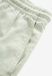 Shorts en coton vert clair avec une taille élastique, présentant une texture fine, des détails cousus et des poches latérales.