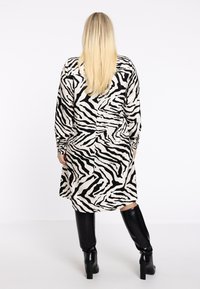 Schwarz-weißes Kleid mit Zebra-Print, langen Ärmeln, lässiger Passform und taillierter Taille, kombiniert mit kniehohen schwarzen Stiefeln.
