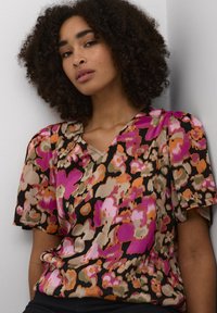Blusa a fiori nei colori rosa, arancione e beige su uno sfondo nero; presenta un collo a V e maniche corte a sbuffo.