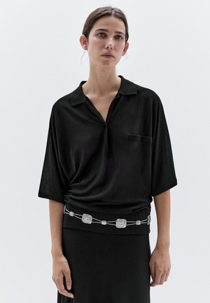Zwart poloshirt met korte mouwen en kraag, met een voorzak en een riem met zilveren accenten. Zachte, gestructureerde stof. Minimalistisch ontwerp.