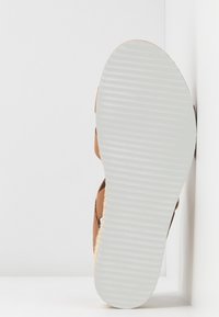 Semelle en cuir marron avec un fond en caoutchouc blanc texturé, accentuée par un style espadrille en jute le long des bords.