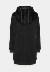 Cappotto in fleece lungo nero con zip, cappuccio, lacci e due tasche laterali con zip, caratterizzato da un tessuto morbido attorno alle spalle e al cappuccio.