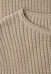 Pull beige en tricot avec un col rond, doté d'un motif côtelé épais et d'un fil texturé doux.