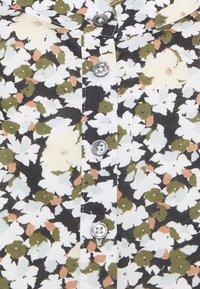 Bloes met bloemenpatroon in zwart, wit en groen met kleine accenten in perzik. Vijf zilveren knopen sieren de voorkant. Van katoen.