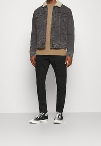 Spijkerjack met schapenvachtkraag, grijze kleur; beige shirt eronder; zwarte cargobroek; zwarte hoge sneakers met witte zolen.