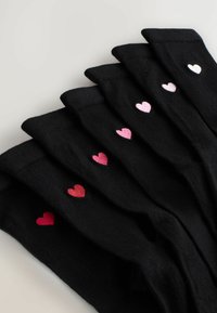 Schwarze Socken in einer Reihe angeordnet, mit unterschiedlich geformten Herzstickereien in verschiedenen Rosa- und Weißtönen. Der Stoff hat eine glatte Textur.