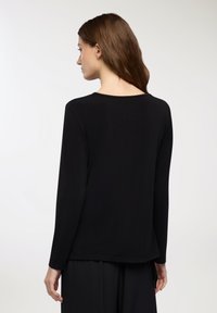 Maglietta nera a maniche lunghe con scollatura rotonda e vestibilità rilassata. Il tessuto appare liscio con una leggera elasticità e senza motivi o dettagli visibili.