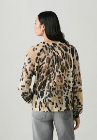 Gebreide trui in beige met een luipaardprintpatroon, voorzien van bruine, zwarte en paarse accenten. Losse pasvorm met lange mouwen en geribbelde randen.