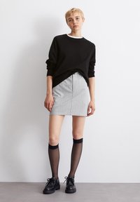 Μαύρο πουλόβερ, γκρι φούστα με κάθετες ρίγες, διαφανείς μαύρες κάλτσες μέχρι το γόνατο και μαύρες παπούτσια με κορδόνια. Απλός, μοντέρνος σχεδιασμός με αντιθετικά χρώματα.