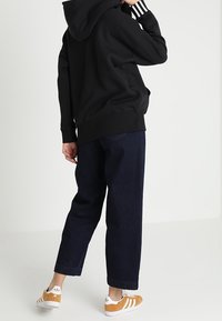 Mustat hupparit, joissa on valkoiset raidat hihansuissa, yhdistettynä tummiin farkkuleikkauksiin ja ruskeilla yksityiskohdilla varustettuihin valkoisiin lenkkarikenkiin. Yksinkertainen, rento asu.