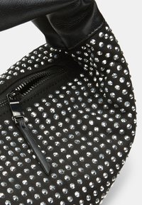 Crna torba od tkanine s srebrnim rhinestones, zatvorenim džepom i glatkom crnom kožnom ručkom. Tekstuirana površina s sjajnim akcentima.