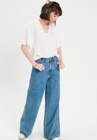 White blouse with short ruffled sleeves and eyelet details, paired with high-waisted blue wide-leg jeans in denim fabric.