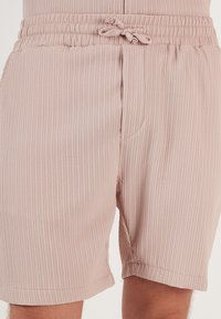Lichtroze, geribbelde shorts met een elastische band en een trekkoord. Bevat zijzakken en heeft een relaxte pasvorm met opgerolde zomen.