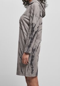 Szara sukienka z kapturem w stylu tie-dye z długimi rękawami, o luźnym kroju, z miękkiego materiału, z unikalnym abstrakcyjnym wzorem wzdłuż rękawów.