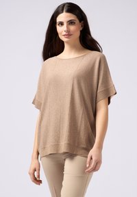 Top beige in maglia con una vestibilità morbida, maniche corte e scollatura rotonda, caratterizzato da un leggero luccichio e orlo a coste. Abbinato a pantaloni beige.