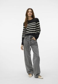 Zwart-wit gestreepte gebreide trui gecombineerd met losse grijze denim broek met een trekkoord in de taille en lichtgekleurde schoenen.