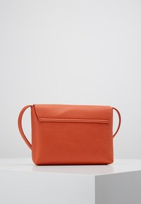 Orange leather crossbody bag with a textured surface, rectangular shape, and a fold-over flap closure. Includes two side handles.