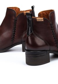 Stivali ankle in pelle marrone con finitura texture, dotati di zip laterale, accenti neri a contrasto e tacco impilato.