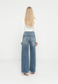 Jeans a vita alta e gamba larga in denim azzurro chiaro, con un lavaggio sbiadito, due tasche posteriori e orlo grezzo. Abbinati a un top bianco aderente.