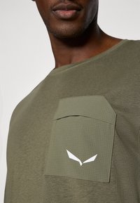 Κοντομάνικο πουκάμισο ελιές με υφή στην τσέπη που διαθέτει ελαφρύ μοτίβο με κουκίδες και λευκό λογότυπο στην τσέπη, από βαμβακερό ύφασμα.