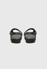 Svart sandaler med stroppdesign, med en polstret såle og teksturert underside. Enfarget med minimale hardware-detaljer.
