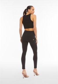 Top corto nero e jeans neri a vita alta, con un design aderente e dettagli di cucitura sottili, abbinati a sandali con tacco nudo.