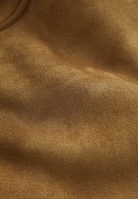 Tissu doux et texturé de couleur marron chaud avec des plis délicats et des fibres fines visibles, mettant en avant sa surface confortable et moelleuse.