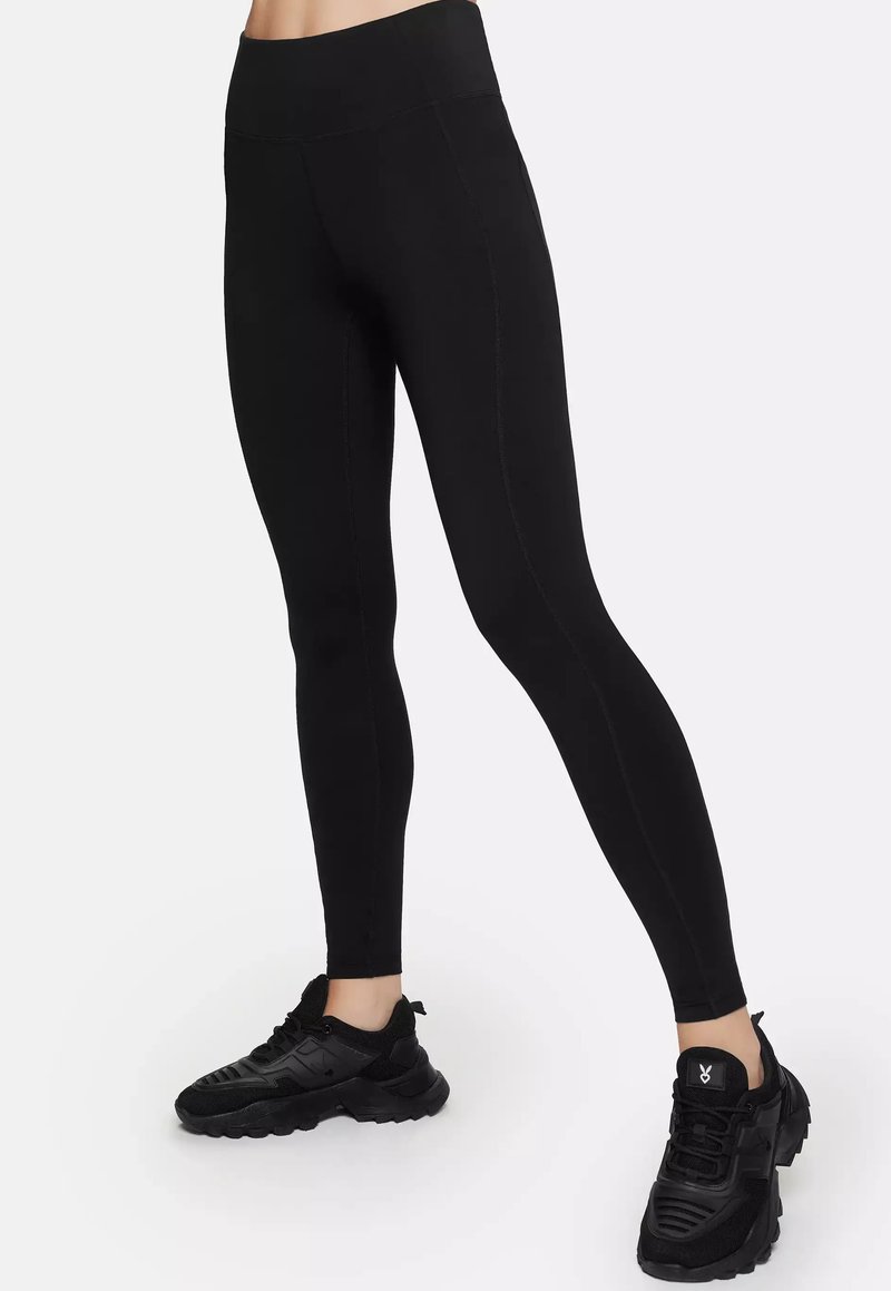 Black leggings with a smooth texture and a high waistband, featuring subtle stitching details. Worn with black athletic shoes.