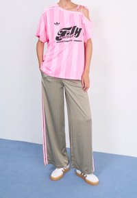Rosa randig oversized T-shirt med off shoulder-design, kombinerad med lösa grå randsydda byxor med rosa sidostripes. Vita sneakers.