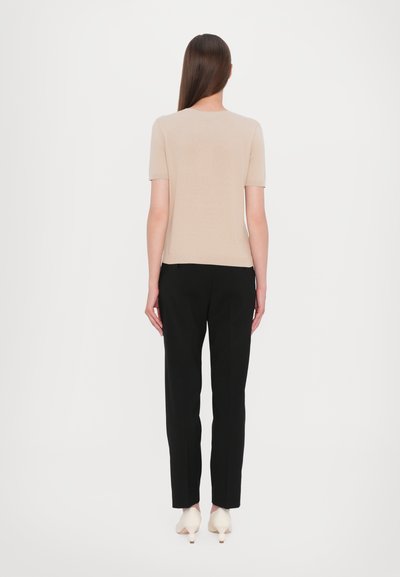 Un top bej cu mâneci scurte, cu un design ajustat, asortat cu o pereche de pantaloni negri croiți și pantofi de culoare deschisă, văzut din spate.
