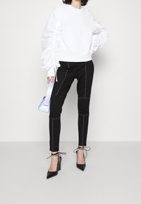 Vit sweatshirt med rynkade ärmar, svarta tajta byxor med kontrastsömmar, och svarta spetsiga klackskor. Liten iriserande handväska.