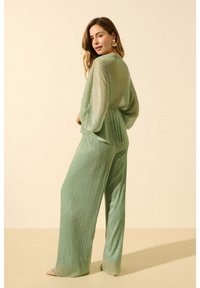 Ensemble en deux pièces plissé vert composé d'un haut à manches longues et d'un pantalon à jambes larges. Le tissu a un léger éclat ; coupe décontractée avec un design fluide.