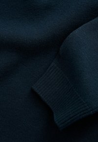 Pull marin foncé avec une texture côtelée fine. Il dispose d'un poignet côtelé et d'un corps lisse, mettant en valeur un matériau tricoté doux.