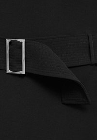 Ceinture en tissu noir avec boucle rectangulaire argentée, montrant une texture cousue et une extrémité repliée sur un fond noir.
