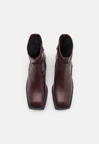 Burgundy läderankelstövlar med fyrkantig tå, sidodragkedja och en texturerad svart gummisula, med en elegant, minimalistisk design.