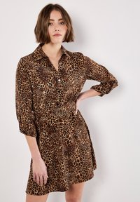 Robe chemise imprimé léopard en marron et noir, avec un col, une fermeture à boutons sur le devant, des manches retroussées et une ceinture avec une boucle en double O.