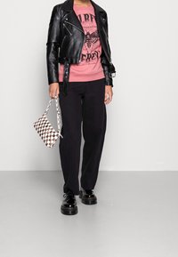 Chaqueta de motociclista de cuero negro recortada sobre un sudadera gráfica rosa, combinada con pantalones de pierna ancha negros y zapatos de plataforma negros. Llevando una bolsa de cuadros.