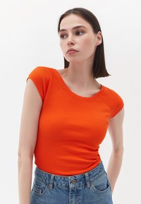 Maglietta arancione a coste con maniche a cappuccio e scollatura rotonda, abbinata a jeans in denim blu a vita alta.