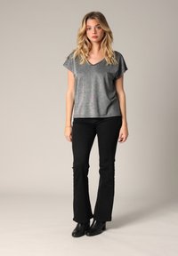 Haut argenté à col en V avec des manches courtes, associé à un jean noir évasé et des bottines noires. Le haut a une texture légèrement scintillante.