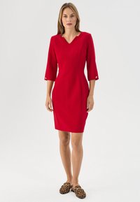 Rotes, tailliertes Kleid mit V-Ausschnitt und Dreiviertelärmeln. Mit maßgeschneiderten Nähten und goldenen Knopfakzenten an den Ärmeln.
