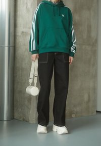 Zelená mikina s bílými pruhy a přední kapsou, doplněná černými širokými džíny. Celek doplňuje bílá kabelka a masivní bílé boty.